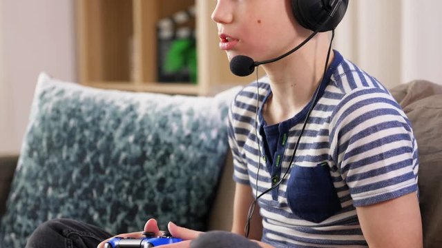 leisure, children, technology and people concept - boy in headphones with microphone and gamepad playing video game at home