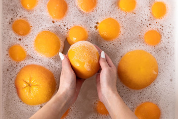 Top view of hands of woman washing ripe orange, grapefruit under faucet in the sink kitchen, soaking fruits in soapy water thoroughly washes after the store. 