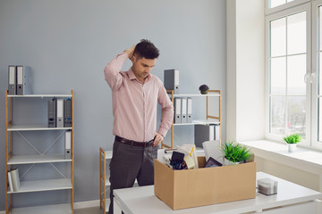 Fototapeta na wymiar Unemployment. Dismissal. Dismissed businessman is upset with a cardboard box holding his head in his hands while sitting in a company office.