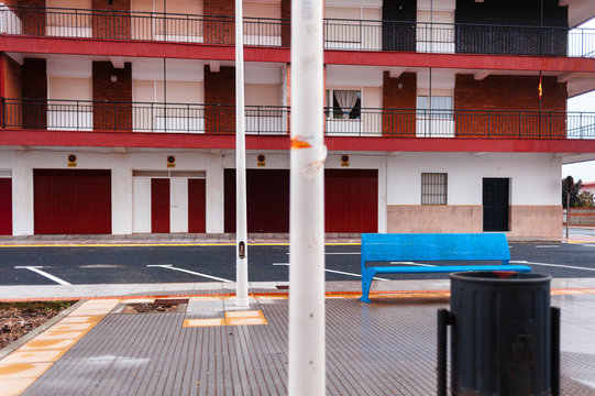Solitary street on rainy day close to  block of flats and blue bench