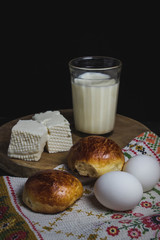 Two homemade buns with a glass of milk. Near two boiled eggs and white homemade cheese