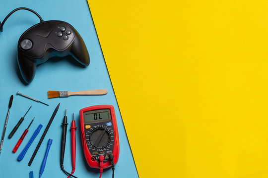 Multimeter, tools and gamepad over blue and yellow background. Concept of diagnosis and technical assistance in electronics and video games. concept of repair and maintenance of amusement machines