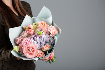 Beautiful bouquet in the hands of a florist. Of roses, carnations, hydrangeas, tulips in brown paper. Flower delivery.