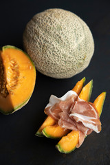 Food concept, prosciutto, ham with fresh melon on a dark background, top view with copy space, with space for your text, italiano snack, flat lay, honey melon or cantaloupe