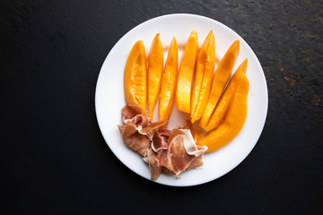 Food concept, prosciutto, ham with fresh melon on a dark background, top view with copy space, with space for your text, italiano snack, flat lay, honey melon or cantaloupe