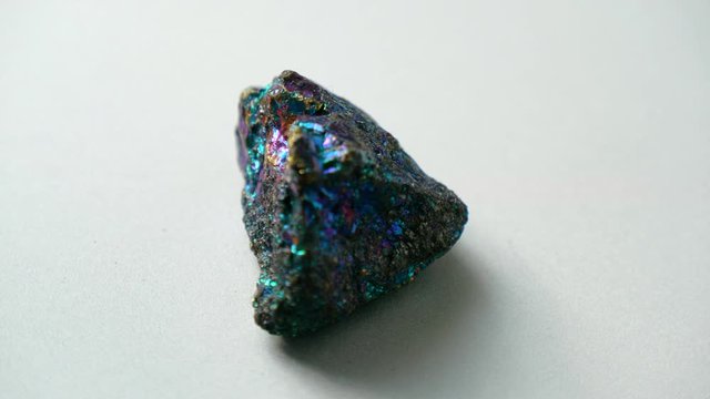 Natural multi-colored green blue chalcopyrite stone spins around its axis on a white stand and white background. Gems, minerals, collection of natural stones, close-ups, study of minerals