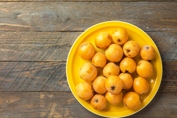 Pile of freshly picked ripe juicy bright orange loquat fruits on bright yellow plate on vintage wooden table top view. Local homegrown produce agriculture vitamins healthy diet concept