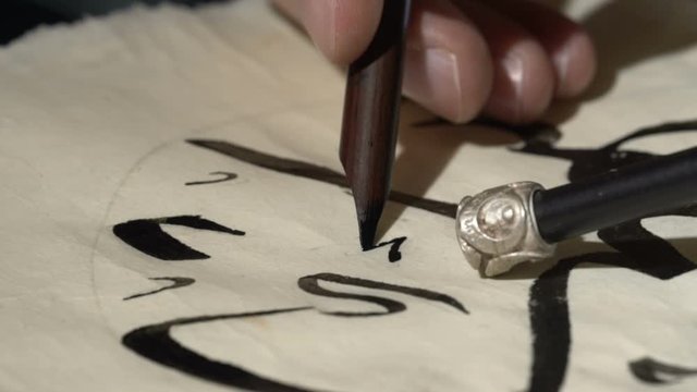 calligrapher writes arabic lettering with calligraphy pen on parchment. macro shot of islamic calligraphy art. close up slider dolly shot in calligrapher workshop
