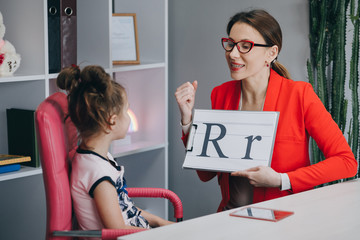 Speech therapist teaches the girls to say the letter R. Speech therapist holding letter R and girl...