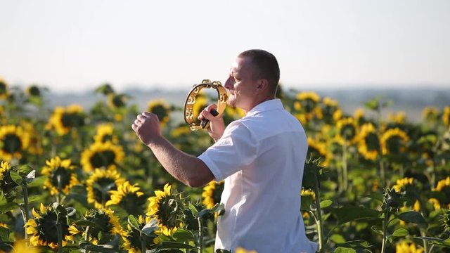 Happy dancer man playing tambourine and dancing energeticly in green summer field.
