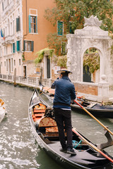 Fototapeta na wymiar Italy wedding in Venice. A gondolier rolls a bride and groom in a classic wooden gondola along a narrow Venetian canal. The back of a gondolier steering a boat with an oar.