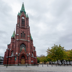 Fototapeta na wymiar Panoramic view of high St. John's Church (Johanneskirken) in Bergen, Norway. Gothic-revival church with red brick & copper details. Cloudy autumn day city tourism