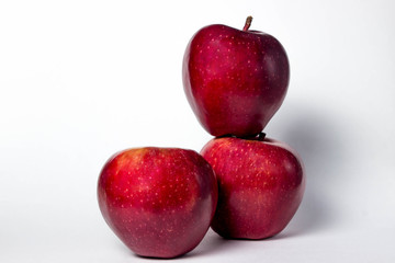 Three red apples on a white background. One apple lies on another apple. The third apple lies ahead