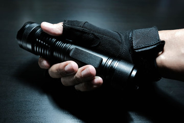 Male hand holding a black metal LED flashlight on a black wooden background 