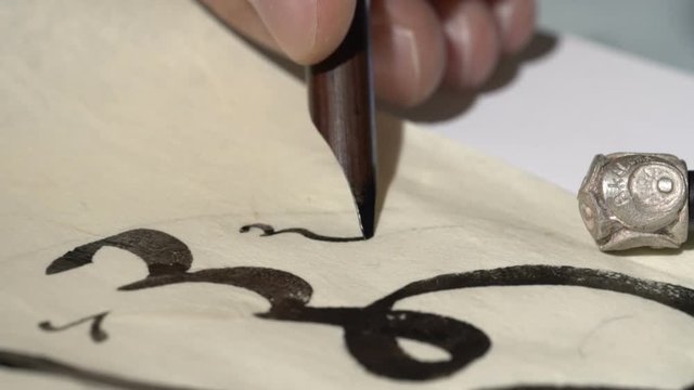 calligrapher writes arabic lettering with calligraphy pen on parchment. macro shot of islamic calligraphy art. close up shot