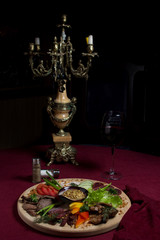 Sliced meat and vegetables on a wooden plate. Nearby is a glass of red wine and an old candlestick.