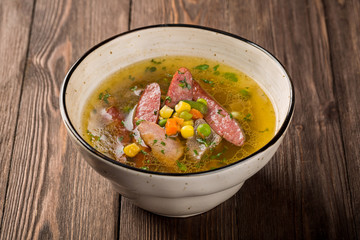 Pea soup with smoked meats in a plate on a wooden background.
