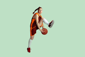 Young caucasian female basketball player in action, motion in high jump isolated on mint colored background. Concept of sport, movement, energy and dynamic, healthy lifestyle. Training, practicing.