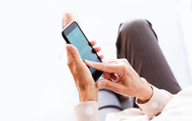 Middle-aged brunette woman on the gray sofa use mobile phone smartphone, surf internet.