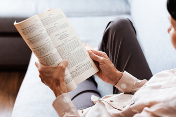 Middle-aged brunette woman on the gray sofa reading book, soft focus, stay at home concept, cozy background.