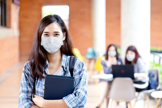 Portrait of young asian student wear mask looking at camera holding notebook or tablet in arm in concept come back or return to school, school reopening and unlock after covid or coronavirus outbreak.