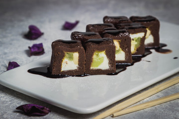 Chocolate rolls poured with chocolate sauce on a white plate. Near Chinese sticks and flower petals