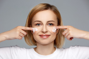 Close up smiling woman apply cream or lotion on face with fingers. Skin care, sunscreen, moisturizing and nourishing. Beauty cosmetic industry