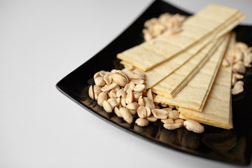 Beer snacks. Long potato chips, salted roasted peeled peanuts in black plate on white table