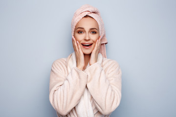 Woman in pink bathrobe with towel on head touching face, after shower at morning, cheerful and ready for new day. Morning beauty routine. Positive lifestyle