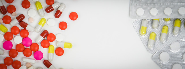 Banner top macro view of colourful medical pills and tablets spilling out of a drug bottle on the white background with copy space.