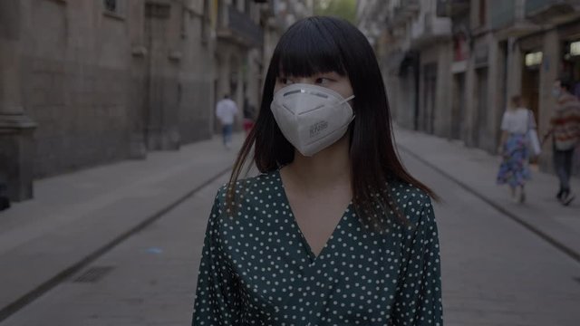 In a pandemic crisis a japanese girl wears a mask while walking through Barcelona city 4K