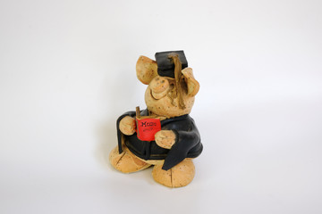 Figure of a ceramic pig wearing a graduation holding a red book with the cover text "MUM" 