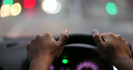 Driver POV hands holding steering wheel waiting. Person hand close-up point of view in red light.