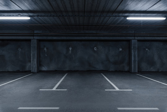 Sci fi looking dark and moody underground parking lot with fluorescent lights on.  Concrete wall