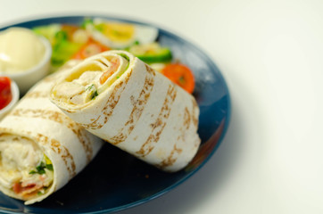 Tortilla wrap with chicken and beechwood smoked bacon served with mix salad on the blue plate
