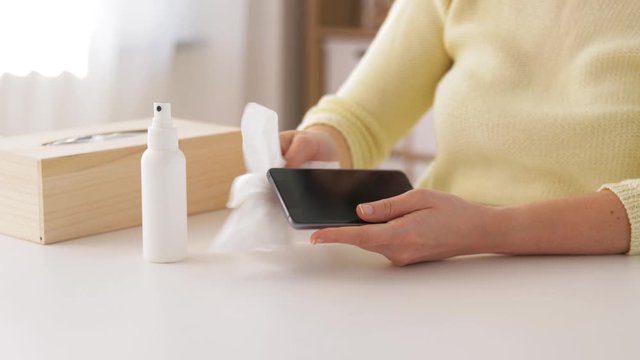 hygiene, cleaning and disinfection concept - close up of woman spraying hand sanitizer to smartphone