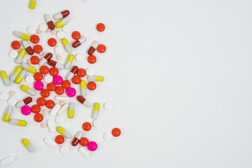 Top view of colourful medical pills and tablets spilled on the white background with copy space.