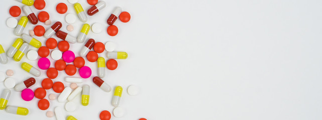 Banner top view of colourful medical pills and tablets spilled on the white background with copy space.