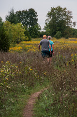 couple man and woman walking on trail through a field of wild flowers