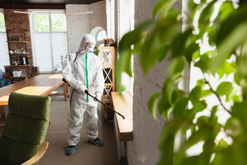 Coronavirus Pandemic. A disinfector in a protective suit and mask sprays disinfectants in house or...