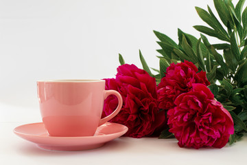 pink cup of coffee and three red peonies on the white background