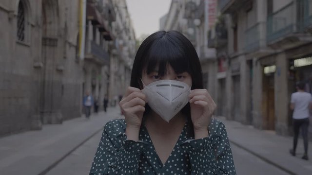 In a pandemic emergency a japanese girl wears a mask while walking through Barcelona city 4K