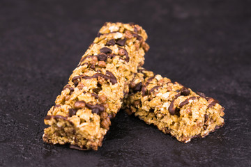 Two fitness granola bars with pieces of chocolate on a black background.