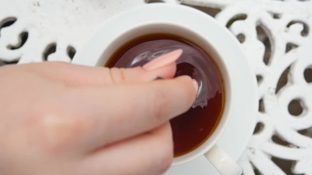 Female hand holds metal spoon and stirs sugar or stevie in a white cup with a herbal tea. Young woman prepares healthy hot drink at breakfast. Concept of tranquility and relax. Top view Slow motion