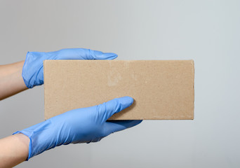Hands with  surgical gloves  of a woman or man holding a cardboard package  .  Protective measures for the distribution of parcels during the covid-19 pandemic .