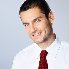 Portrait picture of smiling young confident businessman in white shirt and red tie, against grey background. Square composition.
