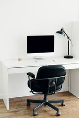 Fototapeta na wymiar White work desk with black monitor, desk lamp and chair. Workplace concept. Minimalism in the interior. Work from home, freelancer workplace.