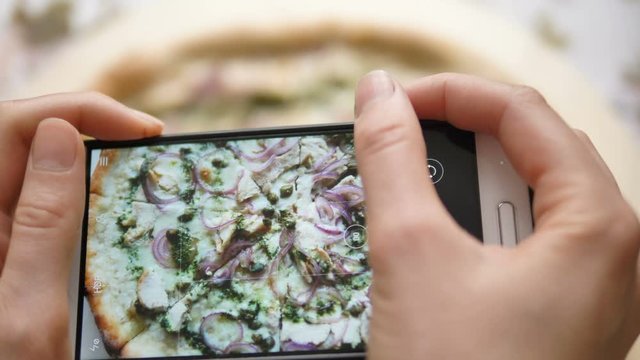 girl takes pictures of fresh pizza on smartphone close-up