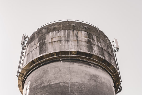 Vertical, high contrast of newly installed 5G cellular antennas seen atop a concrete water tower. Currently in testing phase, to replace existing 4G systems.