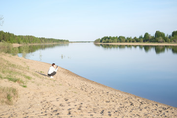 Fototapeta na wymiar woman sitting on the river bank and looking to smartphone. woman in medical mask staying alone outdoors. quarantine end concept. loneliness for balancing mindset. staying alone during quarantine.